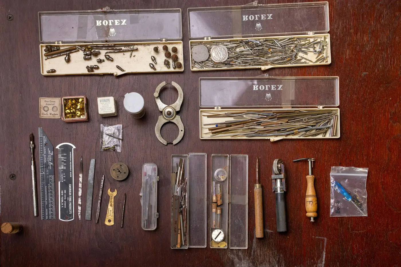 Uhrmacherwerkzeug und Kleinteile in Kunststoffdosen auf einer Holzplatte